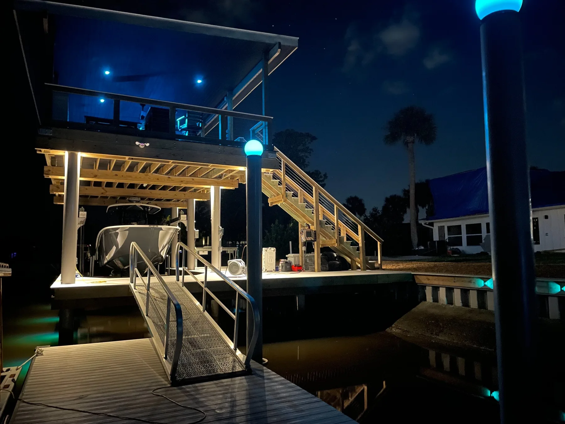 Night view of gangway and boat lift access beside a lit custom dock