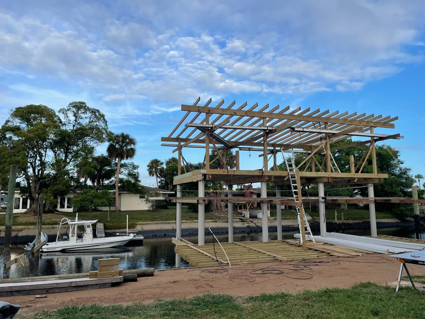 Custom dock under construction with pilings, upper deck framing, and roof rafters