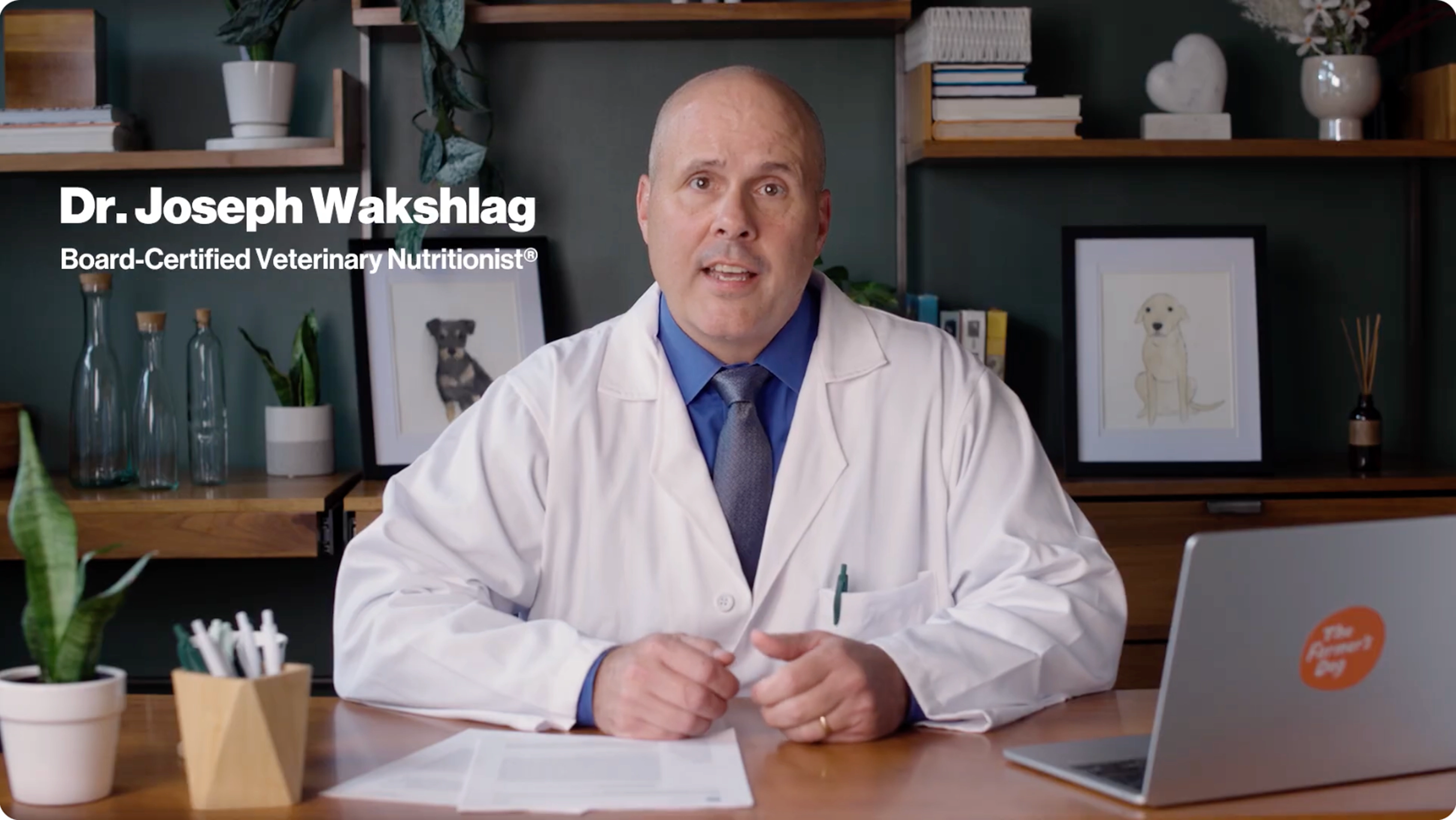 Video thumbnail of Dr. Joseph Wakshlag, board-certified veterinary nutritionist, smiling and sitting at a wooden desk in a white lab coat with stethoscope, in front of bookshelves, plants, dog portrait, laptop, and Farmer's Dog orange logo badge; 2:12 duration overlay.