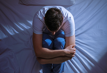 Man hugging his knees alone on bed