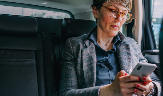 Woman using phone in car. Aura notification bubbles say a new credit account has been detected, and an attempt to access your credit file was blocked.