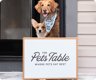 A Golden Retriever and Corgi looking out a door at a The Pets Table delivery box.