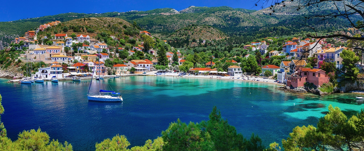 Colorful seaside village surrounding a turquoise bay with boats and green hills.