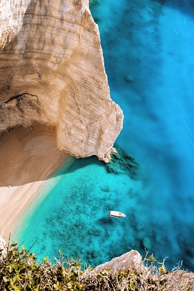 Aerial view of a steep cliff and bright turquoise water with a small boat below.
