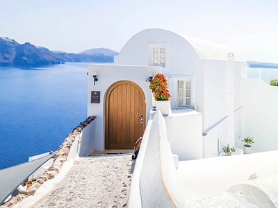 Whitewashed Greek house with stone steps overlooking the blue sea.