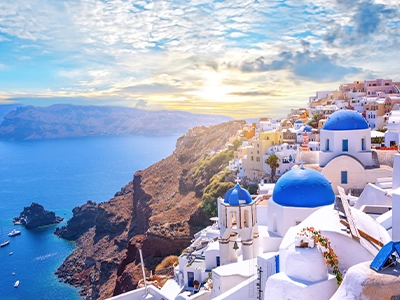 Santorini cliffside with white buildings, blue domes, and ocean at sunset.